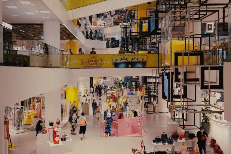Interior movimentado de um shopping center, com consumidores circulando diante de lojas de moda.