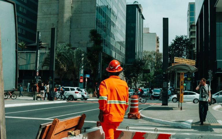 Trabalhador da construção civil em uma movimentada rua de São Paulo, cercado pela atividade urbana.