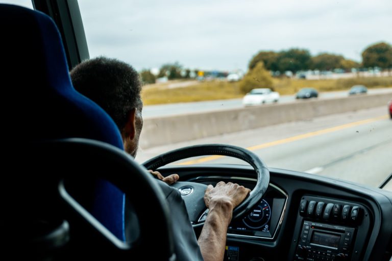 Consulta pública da ANTT ajuda passageiro a identificar transportadoras interestaduais regulares Motorista conduz ônibus em uma rodovia movimentada, com carros ao fundo.